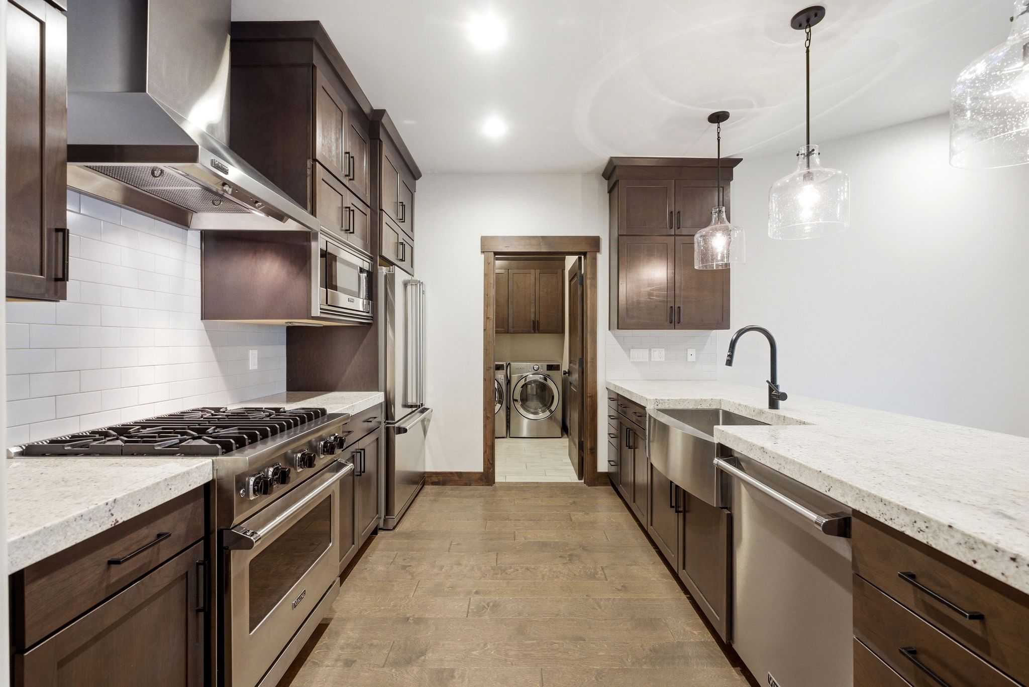 Galley-style kitchen featuring dark wood cabinetry, light-colored countertops, and stainless steel appliances