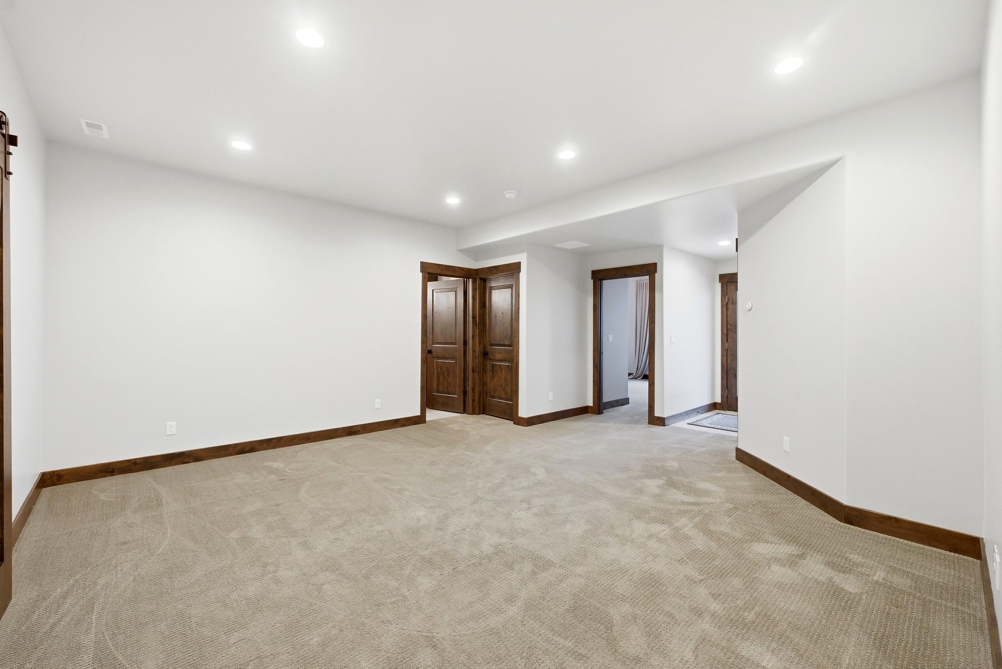 Spacious carpeted room featuring recessed lighting, white walls, and dark wood-finish trim and doors
