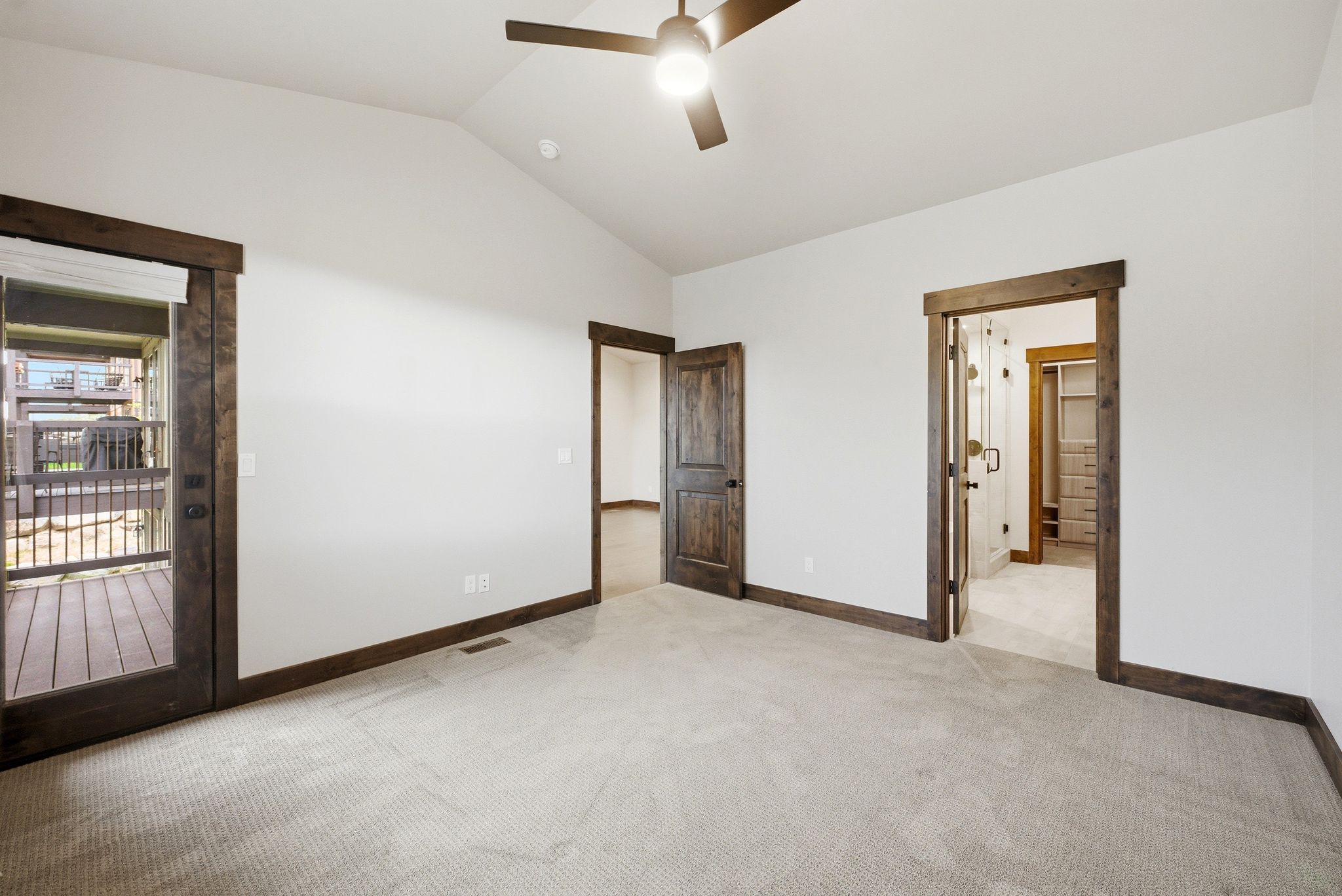 Vaulted ceiling room featuring carpet flooring, dark wood trim, a ceiling fan, and a glass-paneled door opening to an outdoor deck