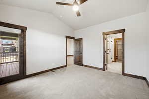 Vaulted ceiling room featuring carpet flooring, dark wood trim, a ceiling fan, and a glass-paneled door opening to an outdoor deck