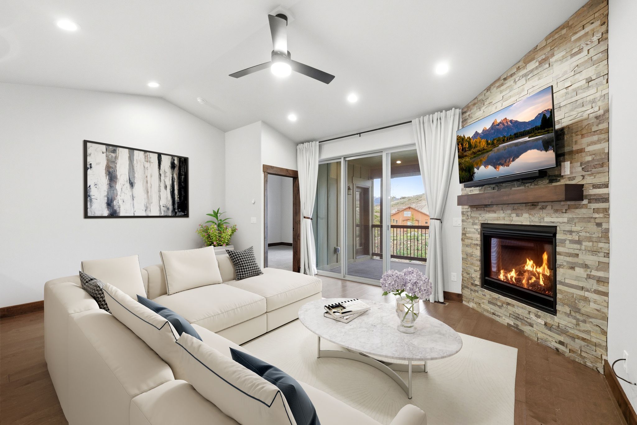 Living area featuring a stacked stone fireplace with a wood mantle, wood-finish flooring, vaulted ceilings with recessed lighting, a ceiling fan, and sliding glass doors opening to a balcony