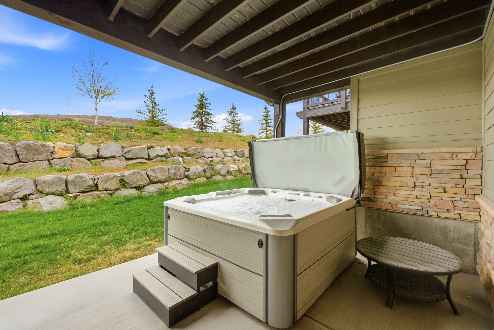 Patio area featuring a built-in hot tub with steps, stone veneer siding, and a concrete slab foundation