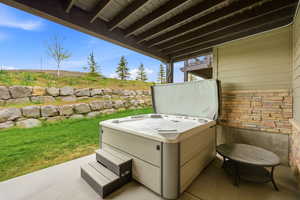Patio area featuring a built-in hot tub with steps, stone veneer siding, and a concrete slab foundation