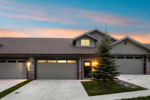 Modern townhome exterior featuring an attached two-car garage, durable siding, stone accents, and a low-maintenance landscape