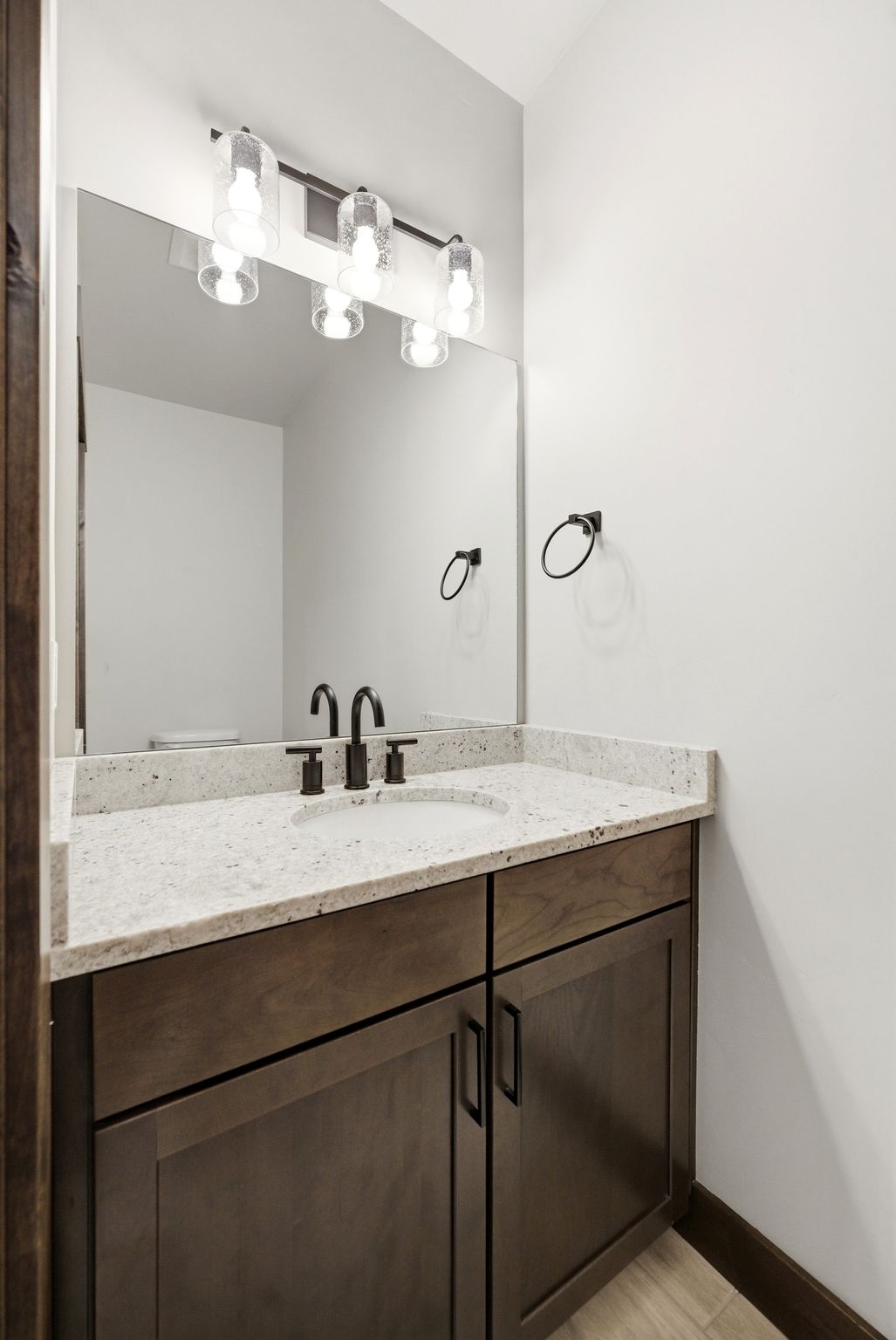 Granite-style countertop with an undermount sink, dark wood-finish vanity, and matte black fixtures