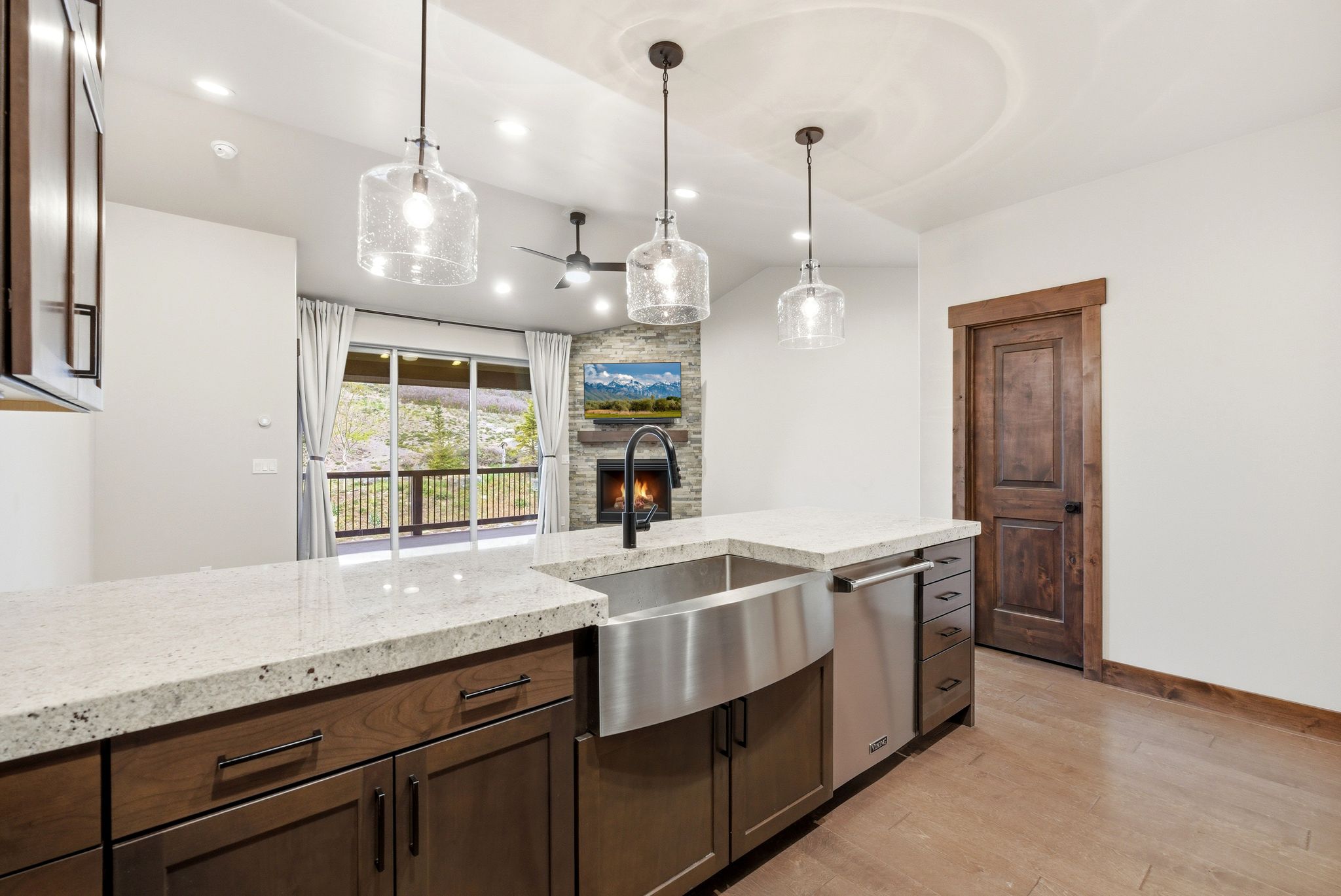 Kitchen island with a stainless steel farmhouse sink, white countertop, and dark wood-finish cabinetry