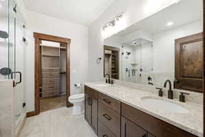 Dual vanity with granite countertops and undermount sinks, matte black fixtures, custom wood cabinetry, glass-enclosed shower, and wood-finish flooring
