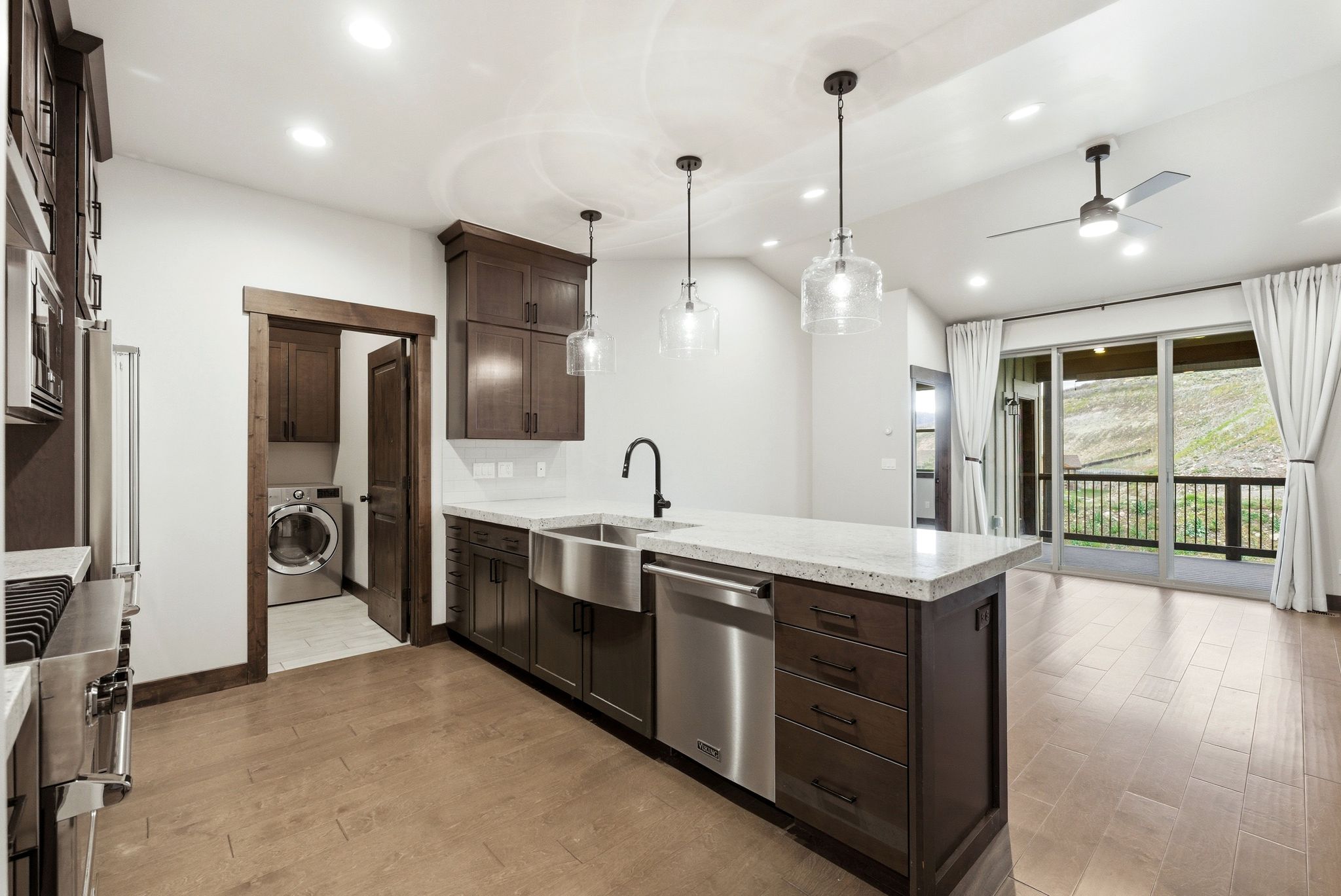 Open-concept kitchen with a large island featuring pendant lighting, integrated stainless steel appliances, and wood-finish flooring extending into the living area