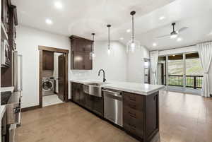 Open-concept kitchen with a large island featuring pendant lighting, integrated stainless steel appliances, and wood-finish flooring extending into the living area