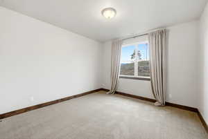 Spacious interior featuring a large window with natural light, light-toned carpeting, white walls, dark wood-finish trim, and a ceiling-mounted light fixture