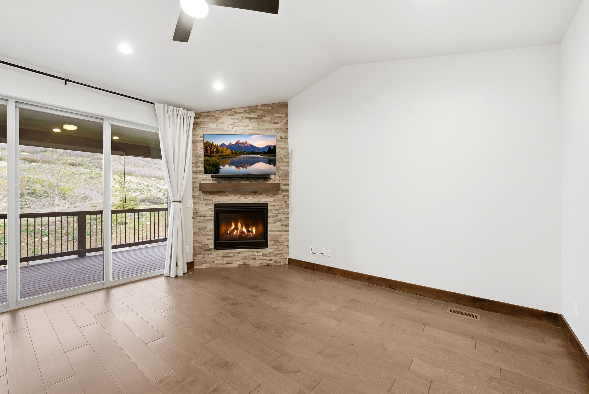 Living area featuring a stone-clad fireplace with a wood mantel, wood-finish flooring, and a ceiling fan
