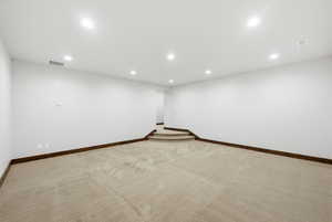 Spacious room featuring neutral carpeting, white walls, dark wood baseboards, recessed lighting, and a carpeted two-step elevation