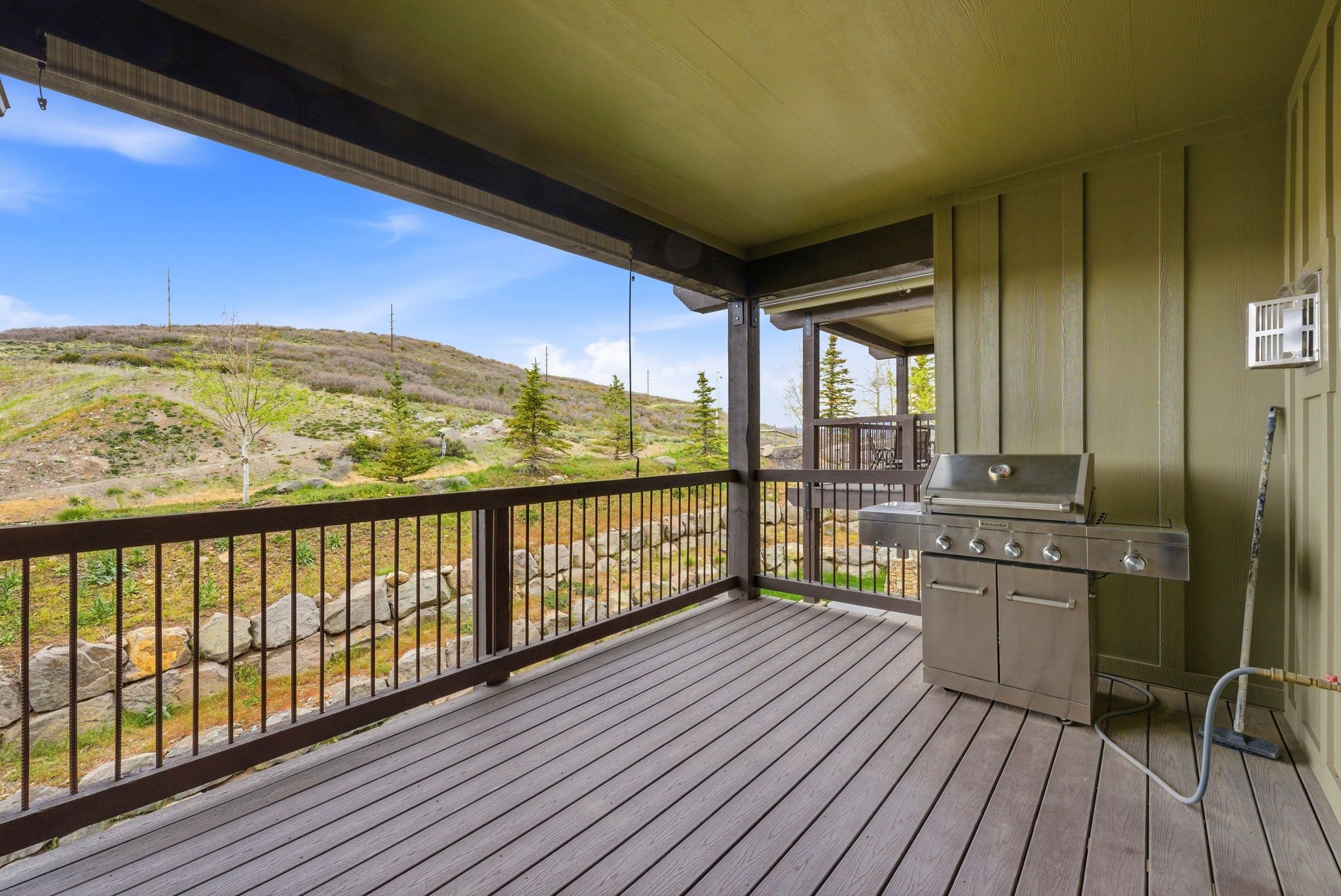 Expansive wood-finish deck with a dark metal railing system, offering panoramic views of the surrounding natural landscape with distant hills and scattered trees