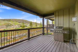 Expansive wood-finish deck with a dark metal railing system, offering panoramic views of the surrounding natural landscape with distant hills and scattered trees