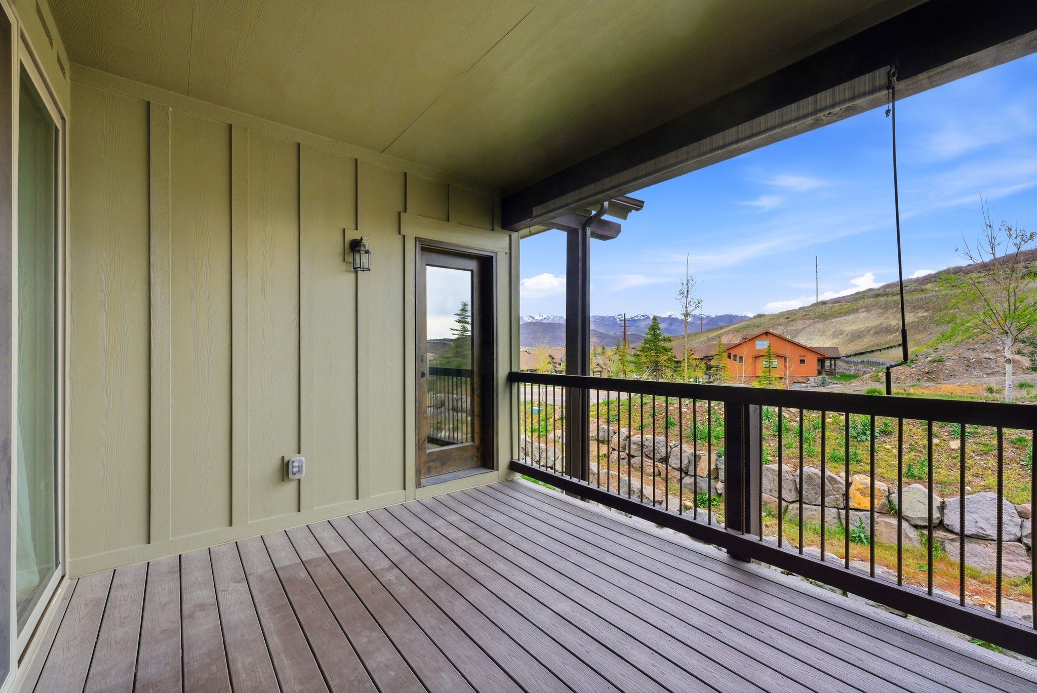 Covered deck featuring wood-finish flooring, vertical plank siding, and a black metal railing