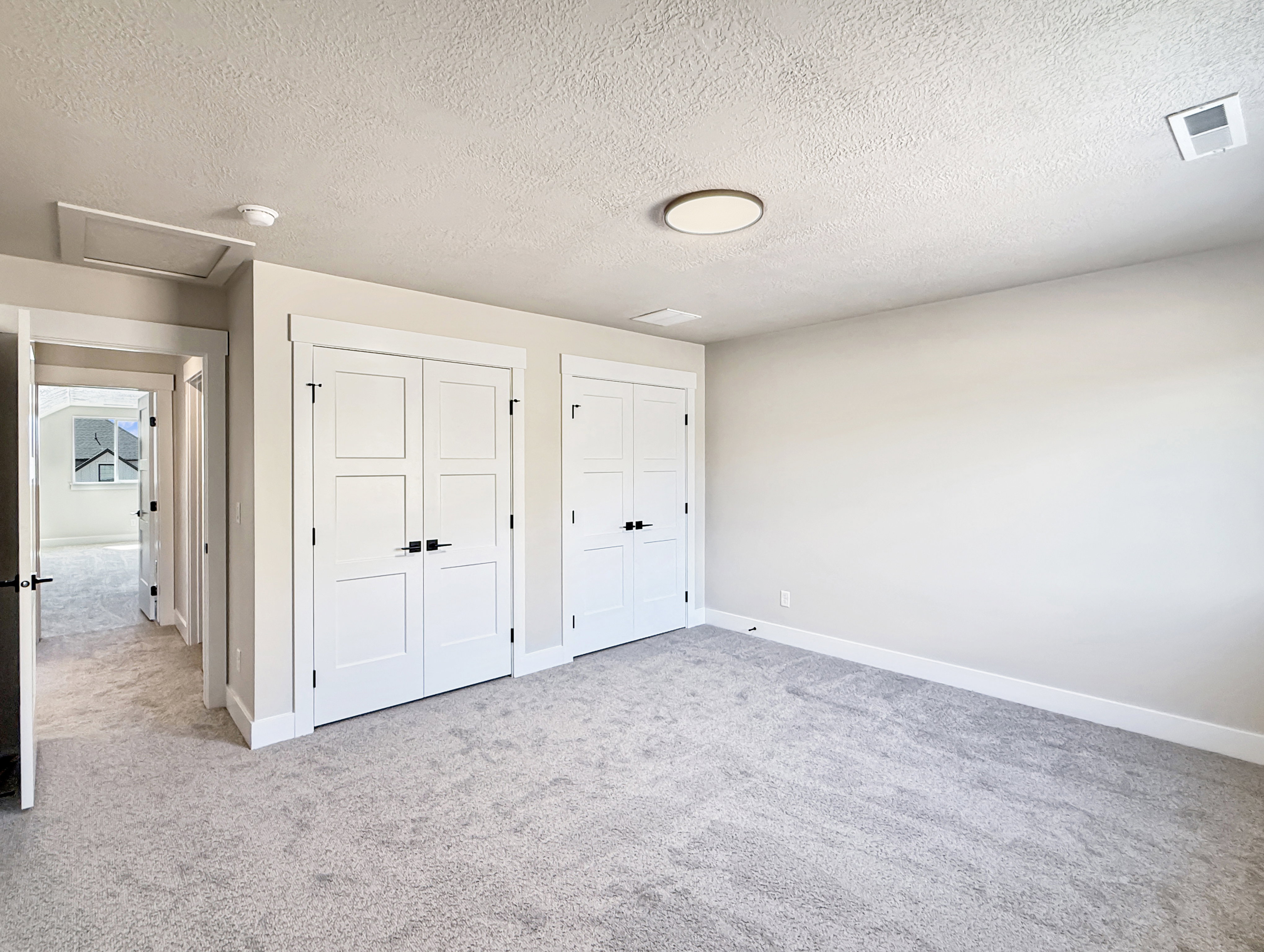 Spacious room featuring light gray carpeting, two sets of white bifold closet doors with dark hardware, and a modern circular flush-mount ceiling light