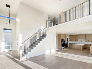 Open-concept living space featuring high ceilings, wood-finish flooring, a contemporary black metal chandelier, and a staircase with light wood handrails and black balusters