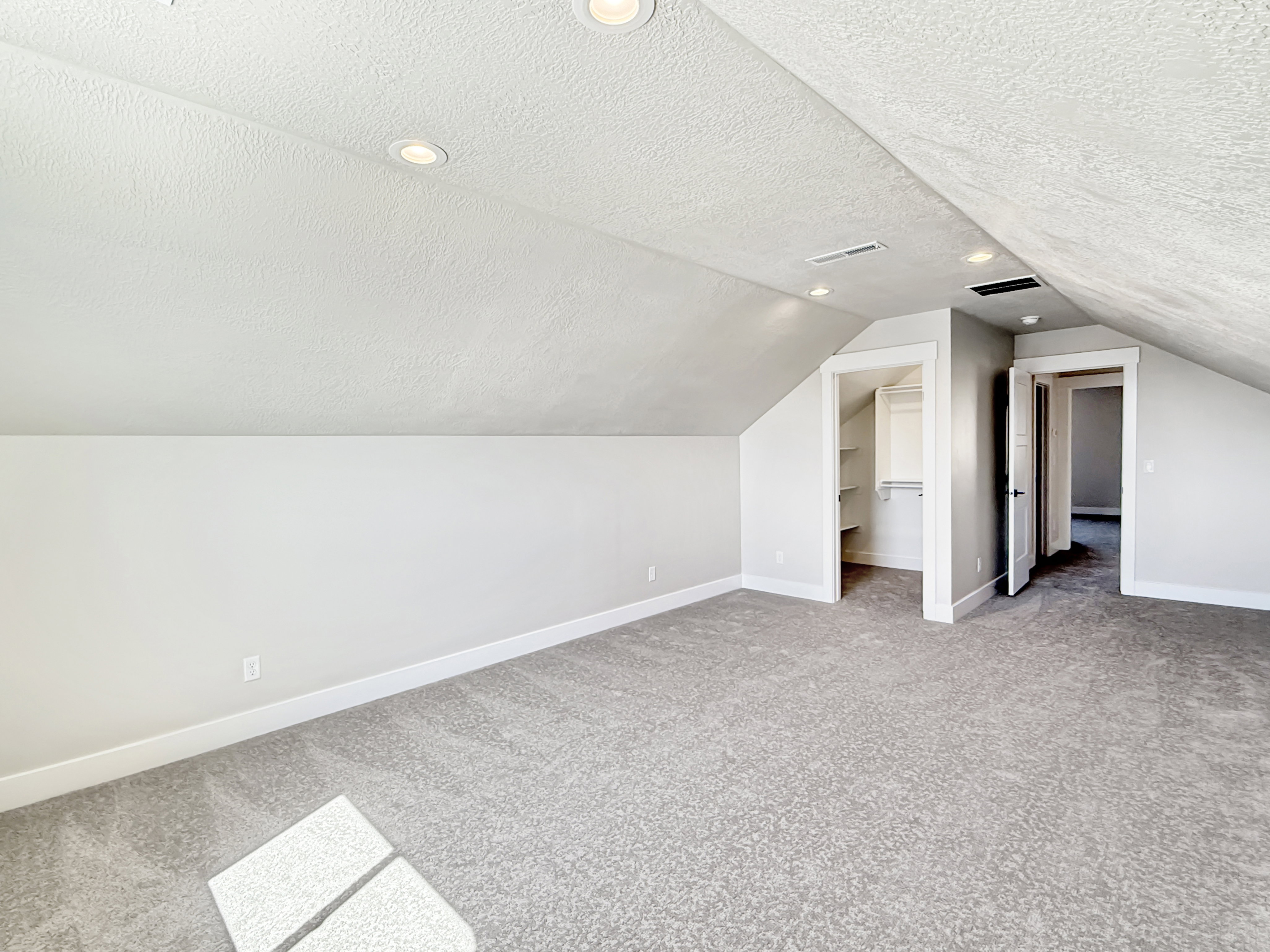 Spacious finished attic area featuring sloped ceilings, recessed lighting, neutral tone carpeting, and two integrated doorways