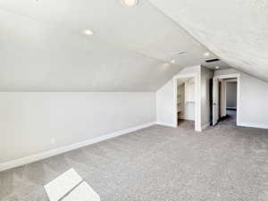 Spacious finished attic area featuring sloped ceilings, recessed lighting, neutral tone carpeting, and two integrated doorways