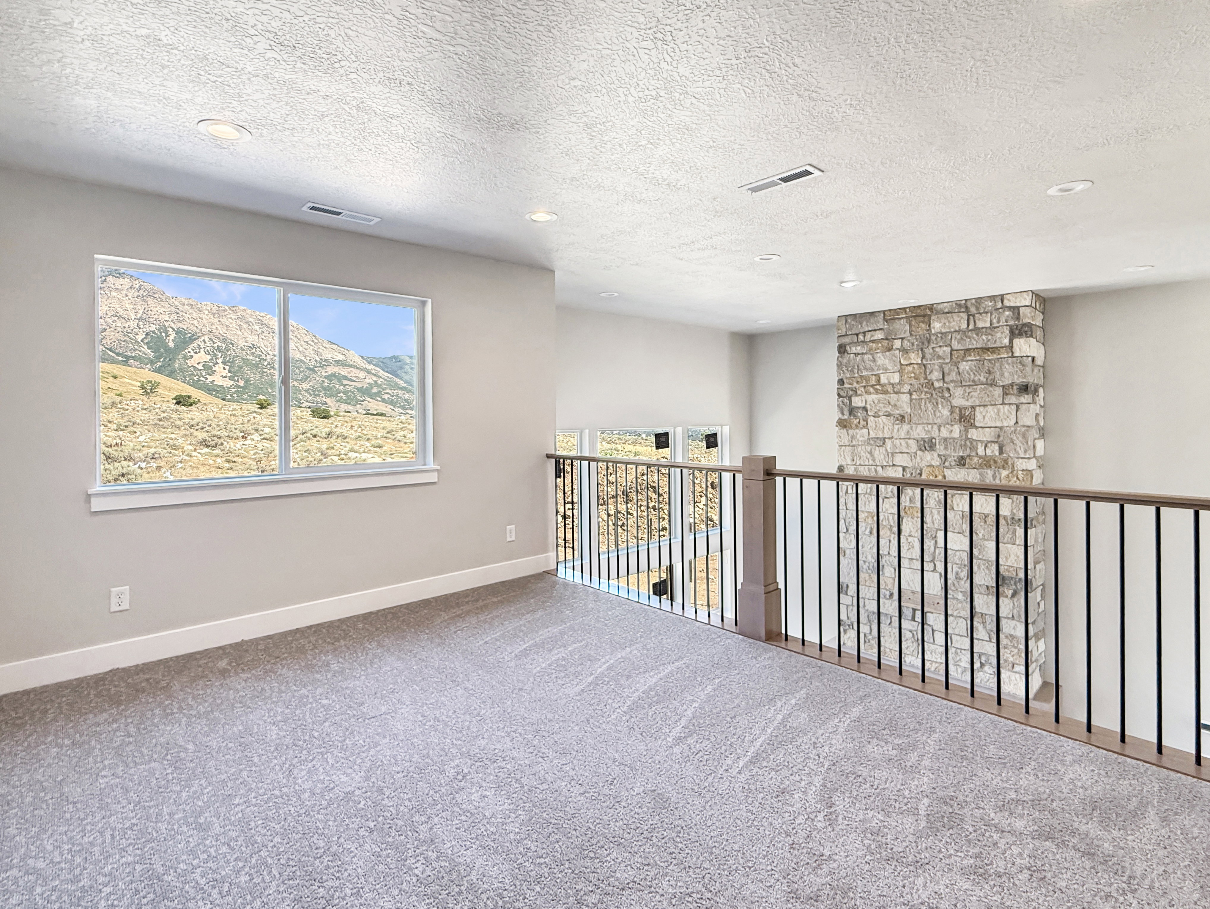 Carpeted loft area featuring a large window, recessed lighting, and a stacked stone accent wall