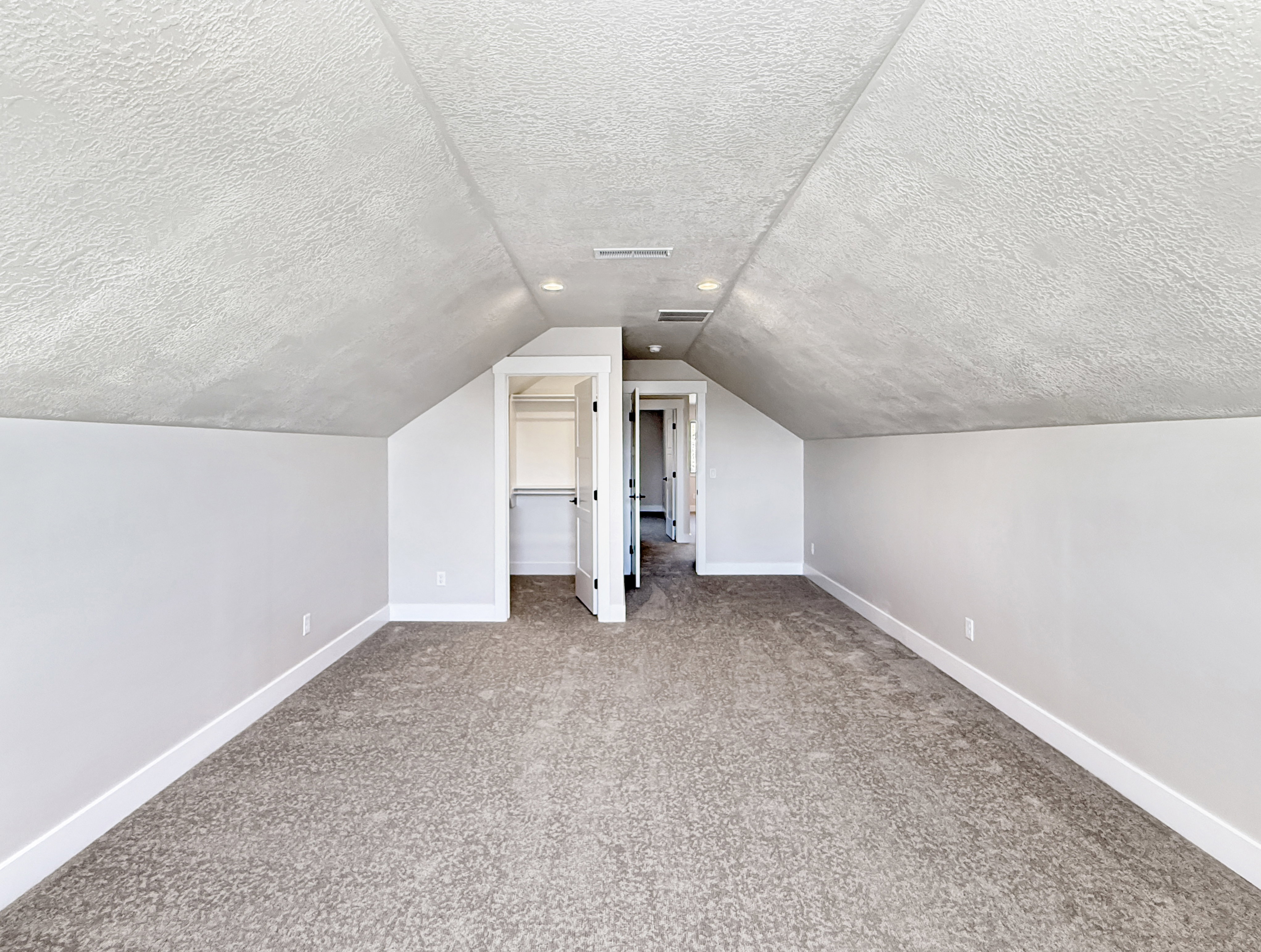 Spacious attic room featuring sloped ceilings, textured wall finishes, recessed lighting, and soft carpet flooring