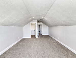 Spacious attic room featuring sloped ceilings, textured wall finishes, recessed lighting, and soft carpet flooring