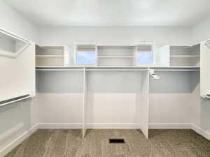 Spacious walk-in closet featuring white built-in shelving, multiple hanging rods, and light-colored carpeting