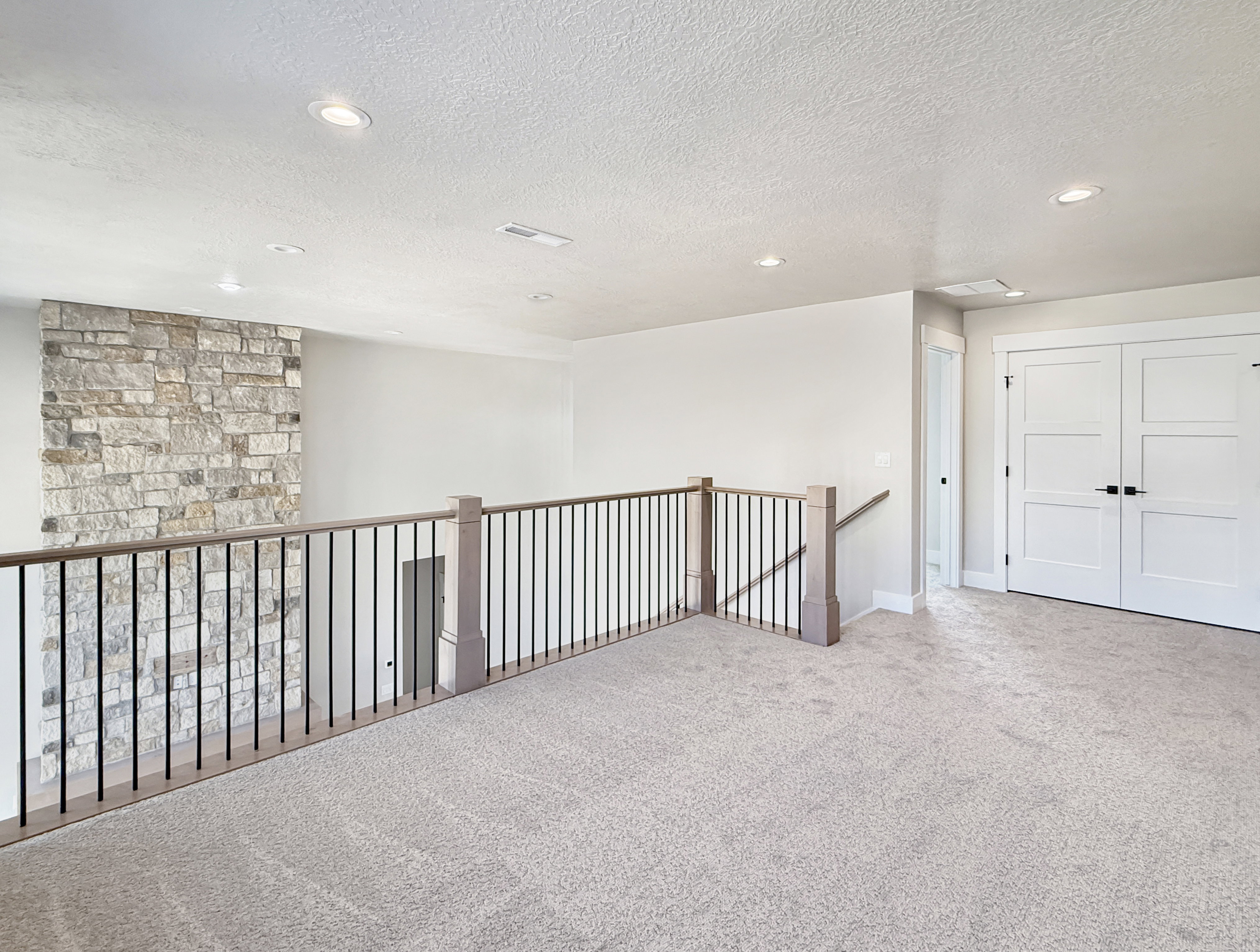 Expansive loft area featuring neutral carpeting, recessed ceiling lighting, and a stone accent wall