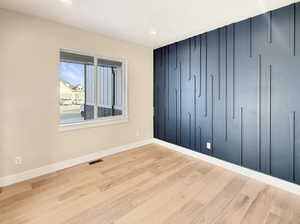 Feature wall with geometric paneling, recessed lighting, wood-finish flooring, white trim, and a window with white casing