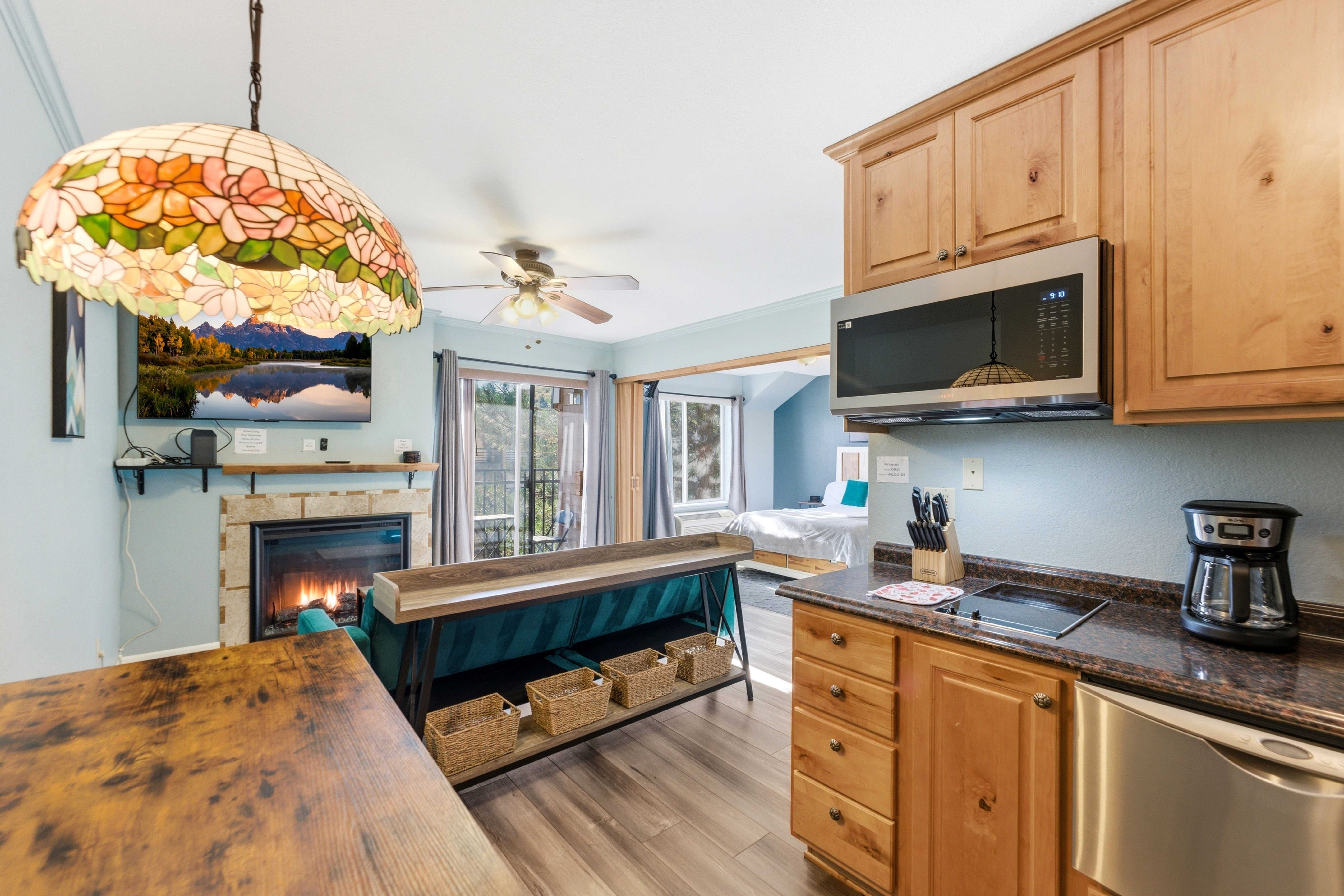 Open-concept living area with wood-finish flooring, a stone-faced fireplace with a wooden mantel, and a stained-glass pendant light fixture