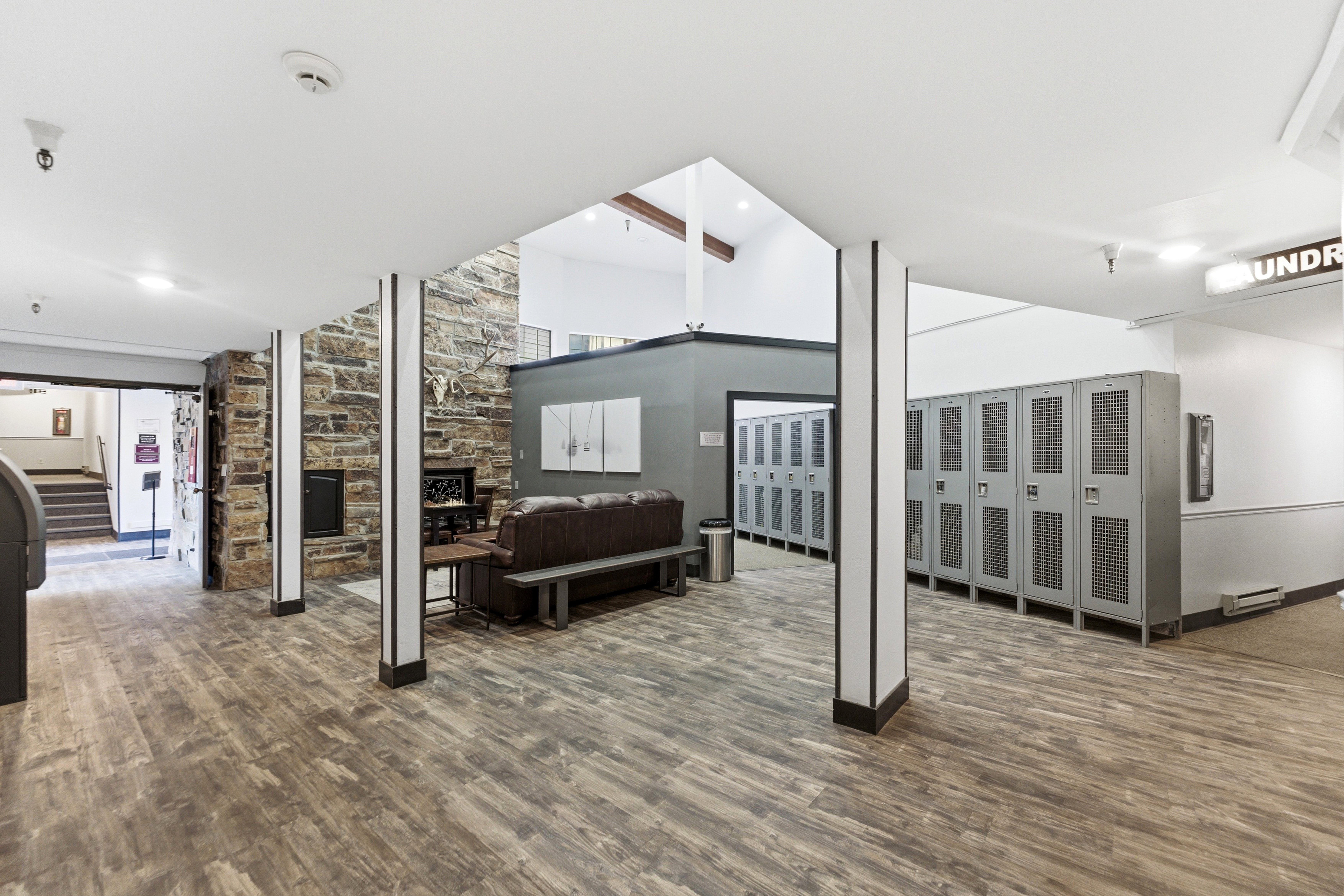 Spacious common area featuring wood-finish flooring, a stone accent wall with a built-in fireplace, and a high vaulted ceiling