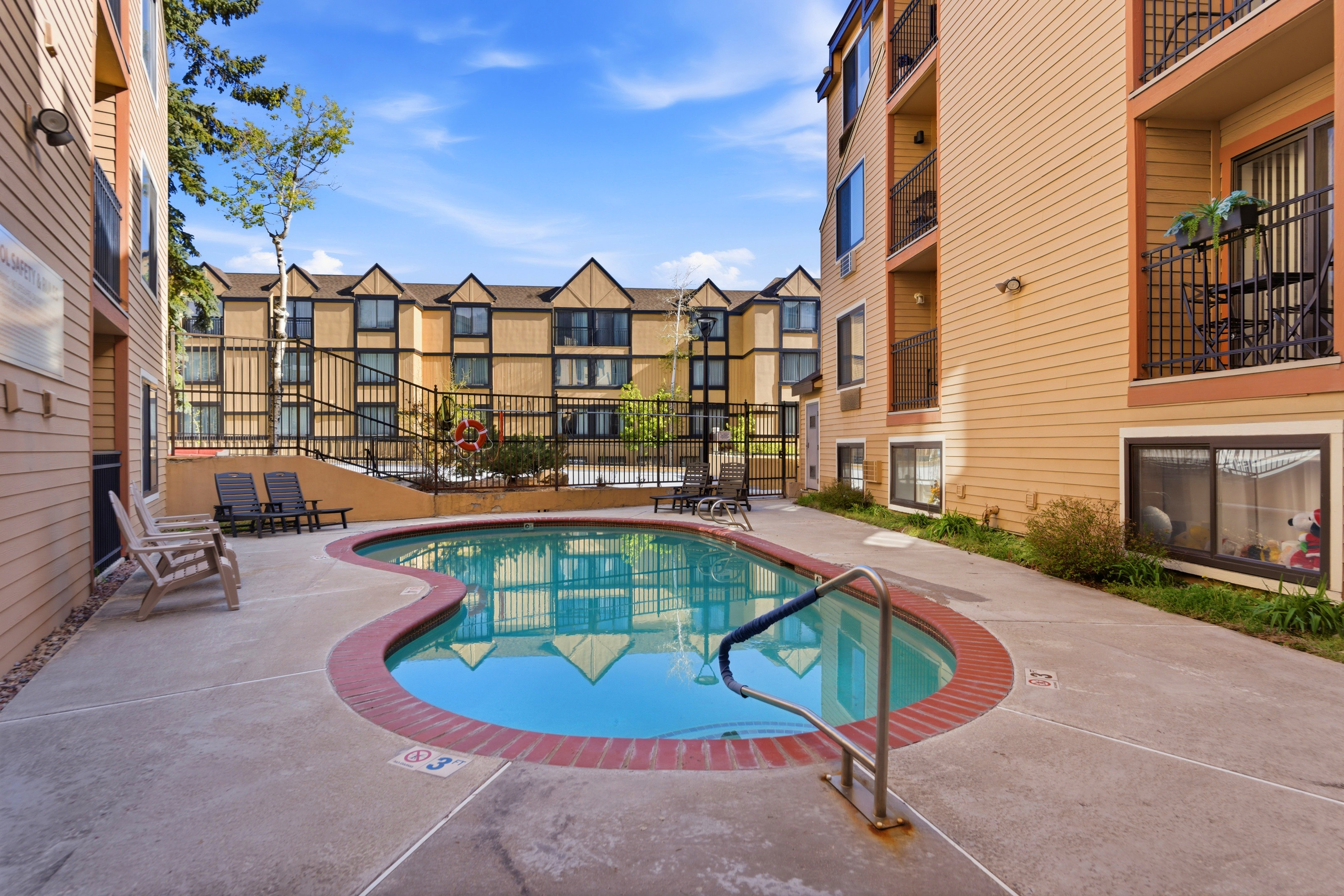 Curved outdoor pool with a red brick coping, surrounded by a concrete pool deck