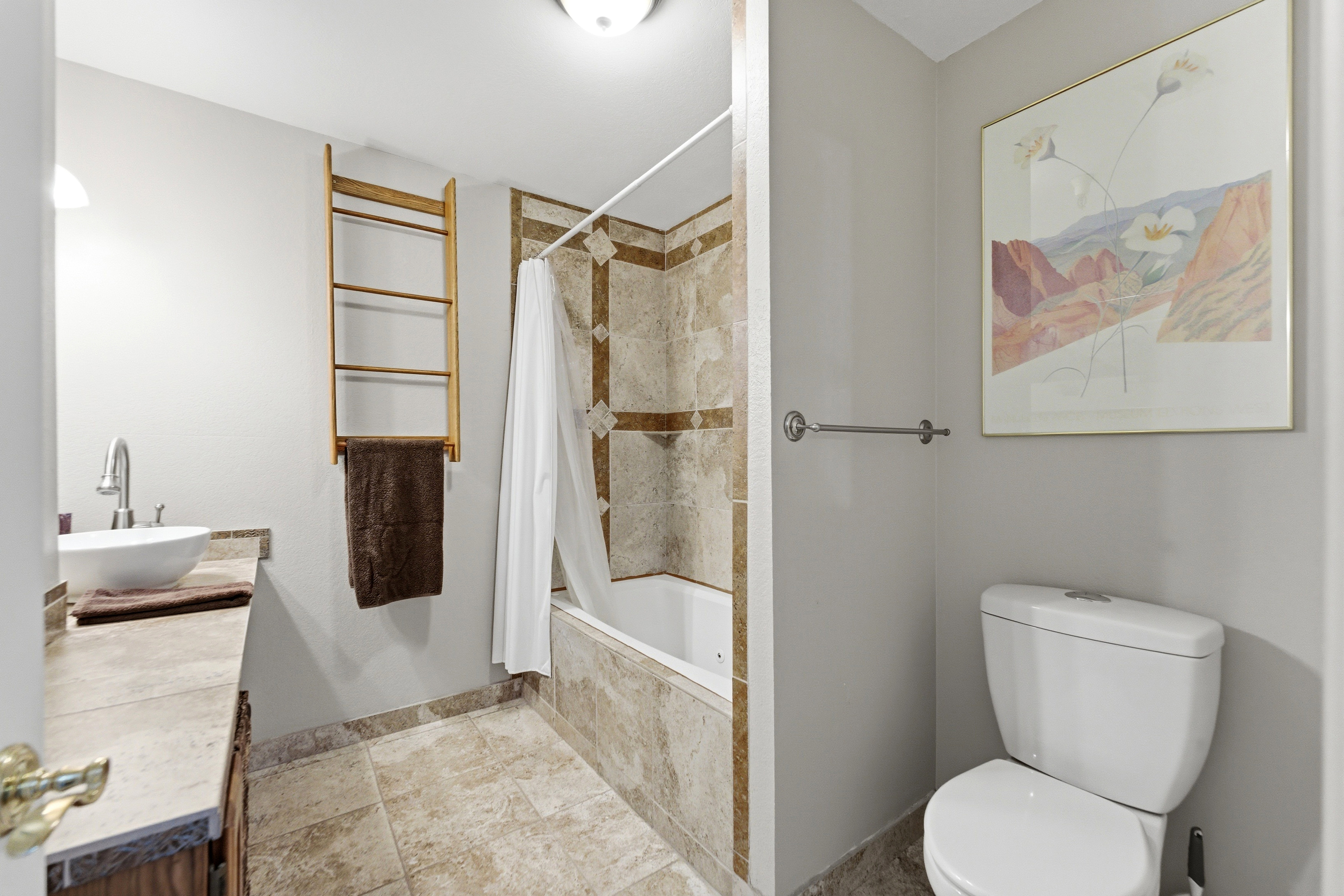 Bathroom featuring a white vessel sink, stone-look countertop, integrated bathtub, and coordinated stone-look tile flooring