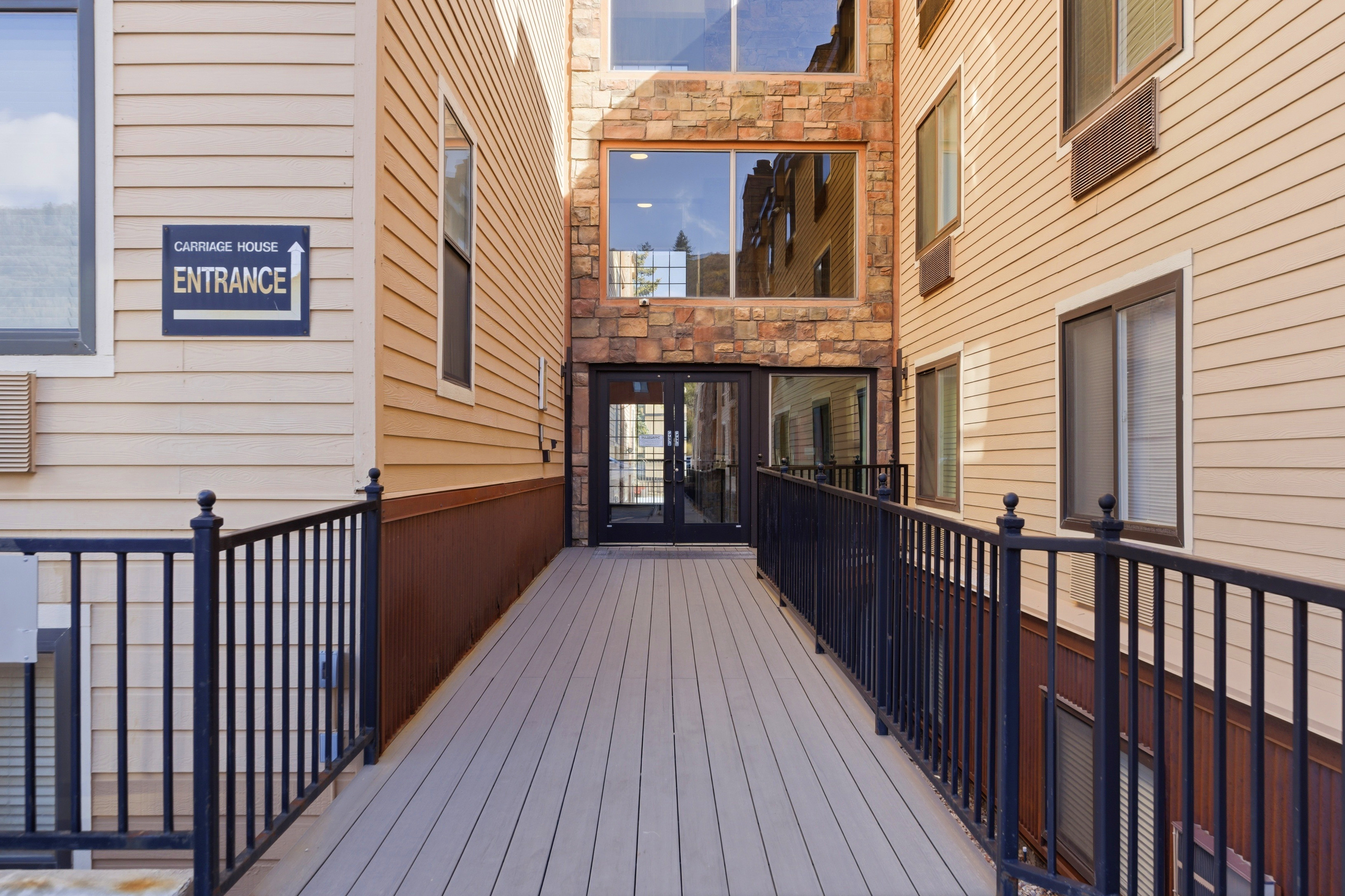 Exterior entrance ramp with dark metal railings, leading to glass doors framed by stacked stone and large windows