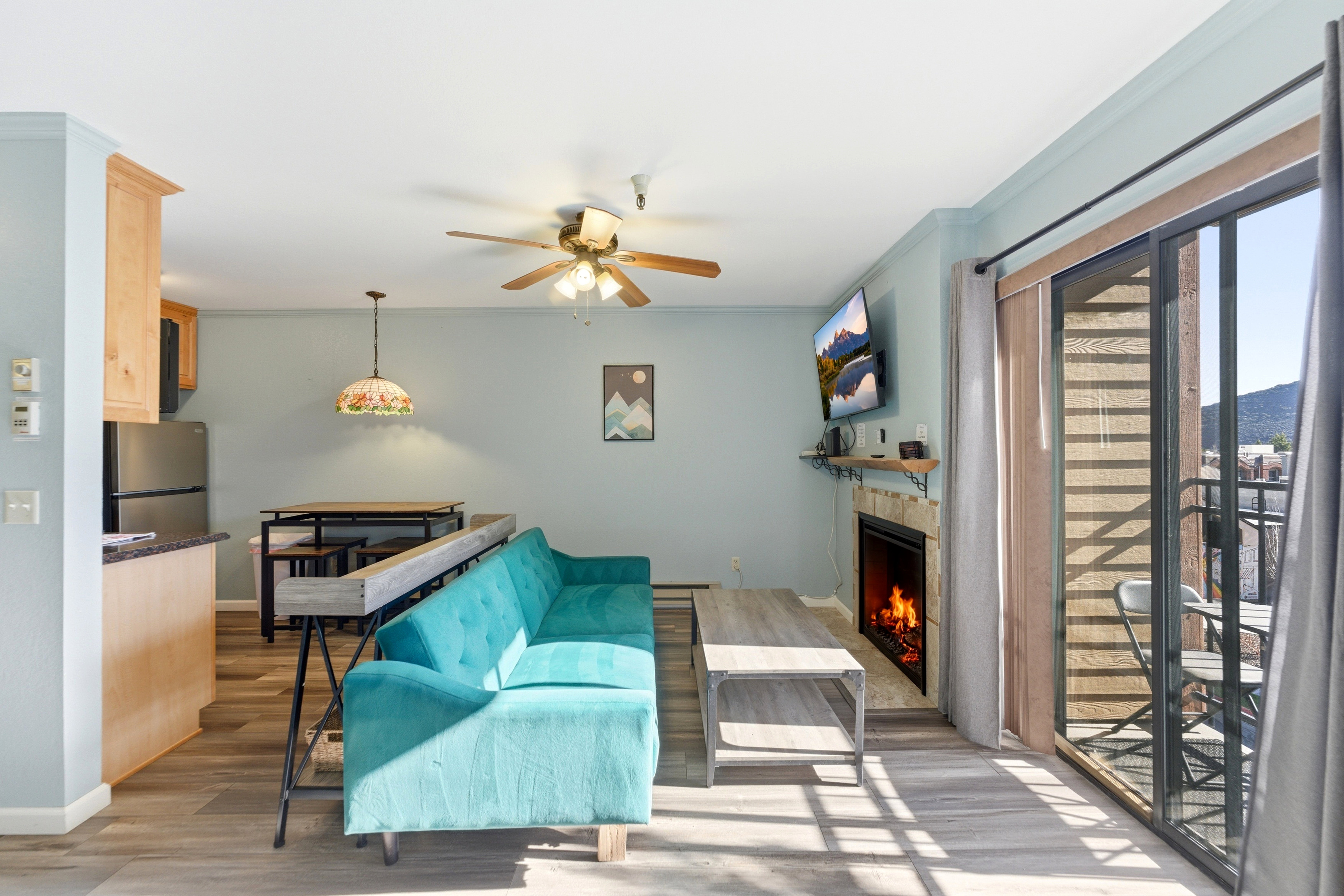 Open-concept living space featuring wood-finish flooring, a ceiling fan with integrated lighting, and a built-in fireplace with a stone-tile surround and wood mantel