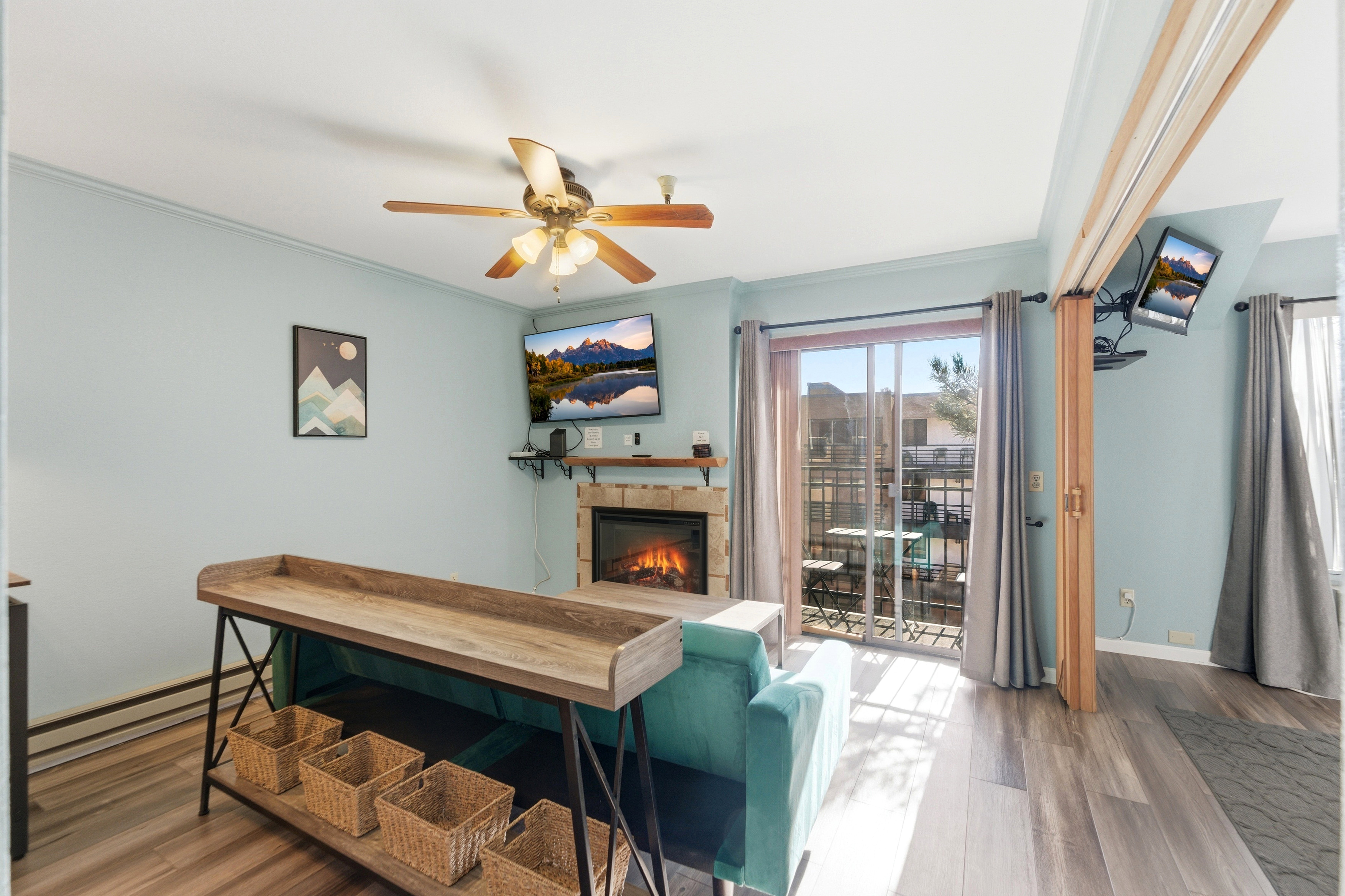 Living area featuring wood-finish flooring, a ceiling fan with integrated lighting, and a stone-clad fireplace with a built-in mantel