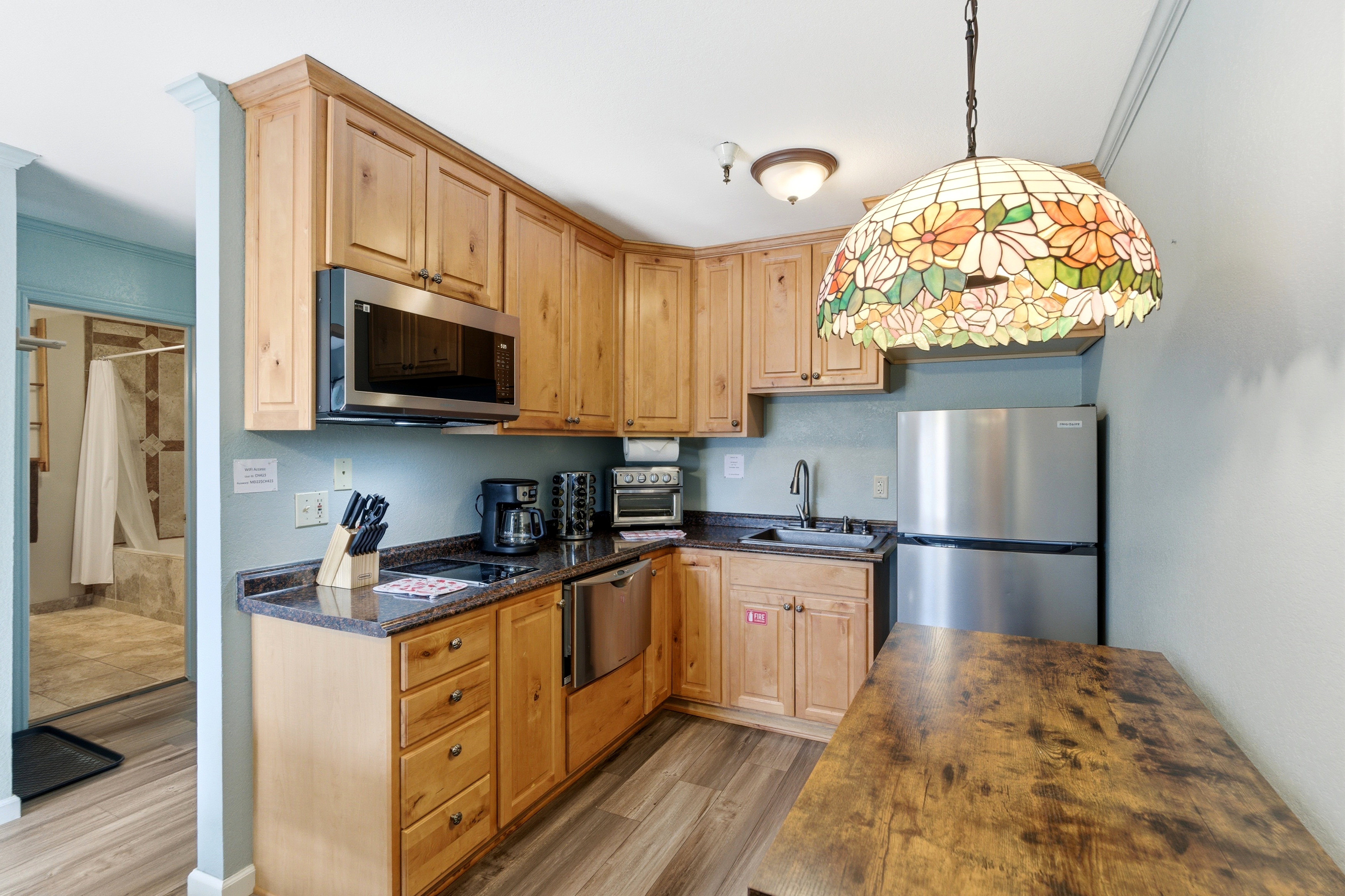 Kitchenette featuring wood-finish cabinetry, dark countertops, stainless steel appliances, and wood-finish flooring