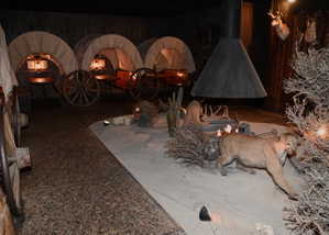 Interior space featuring a desert-themed display with multiple covered wagons, a freestanding conical fireplace, and a simulated sandy terrain