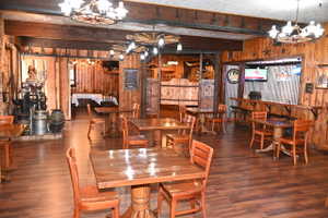 Spacious common area featuring wood-finish flooring, wood paneling, exposed wood beams, and wagon wheel light fixtures