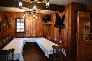 Wood-paneled room featuring a U-shaped table setup, wagon wheel chandeliers, wood-finish flooring, and a window with wood blinds