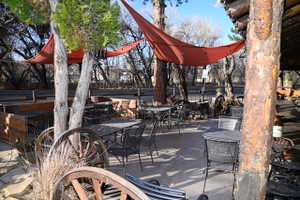 Outdoor patio area featuring multiple seating arrangements, two overhead fabric shade structures, a prominent log column, and decorative wagon wheels