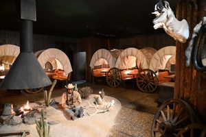 Themed interior space featuring multiple covered wagon structures, a central freestanding metal fireplace, and textured wall finishes