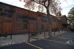 Rustic wood-clad facade featuring multiple storefronts with distinct signage, a gravel perimeter, and a paved parking area