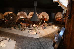 Themed interior space featuring multiple covered wagon installations, a central free-standing fireplace with a conical hood, and a simulated desert landscape with various decorative elements