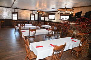 Spacious dining area featuring wood-finish flooring, pressed tin wall panels, a wagon wheel chandelier, multiple windows, and a decorative wagon display