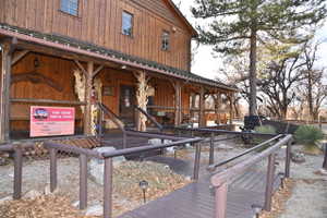 Exterior featuring a rustic wood-plank facade, a covered porch with log-style supports, dark wood-finish decking, an accessible ramp with railings, and established landscaping with mature trees