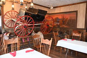Interior space featuring a wagon display with red spoked wheels, rustic wood paneling, a large desert mural, and lantern-style light fixtures