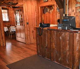 Rustic wood-paneled interior featuring a prominent reception counter with a live-edge wood top, wood-finish flooring, and a paneled door with glass inserts leading to an additional space