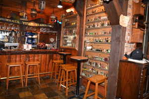 Custom-built bar area featuring a wood-plank bar front with a foot rail, a multi-shelf display case, and recessed lighting