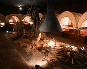 Thematic interior space featuring multiple covered wagon structures, a central display with simulated desert landscaping, an overhead metal hood, and integrated lighting